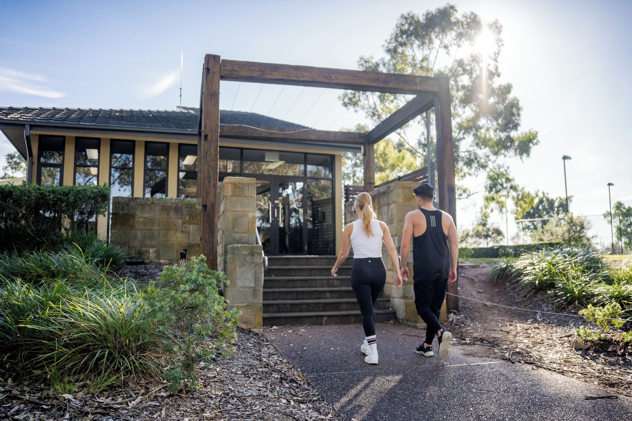 Two people walking towards a building with a stone facade and a wooden archway.