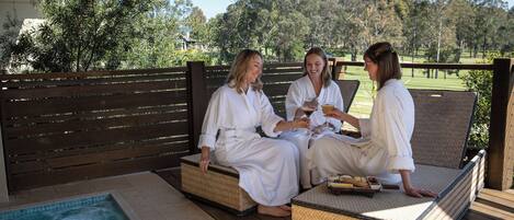 Three people sitting on wicker lounge chairs by a hot tub, with a view of a golf course in the background.