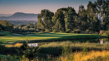 Un campo da golf con uno stagno, alberi e montagne sullo sfondo.