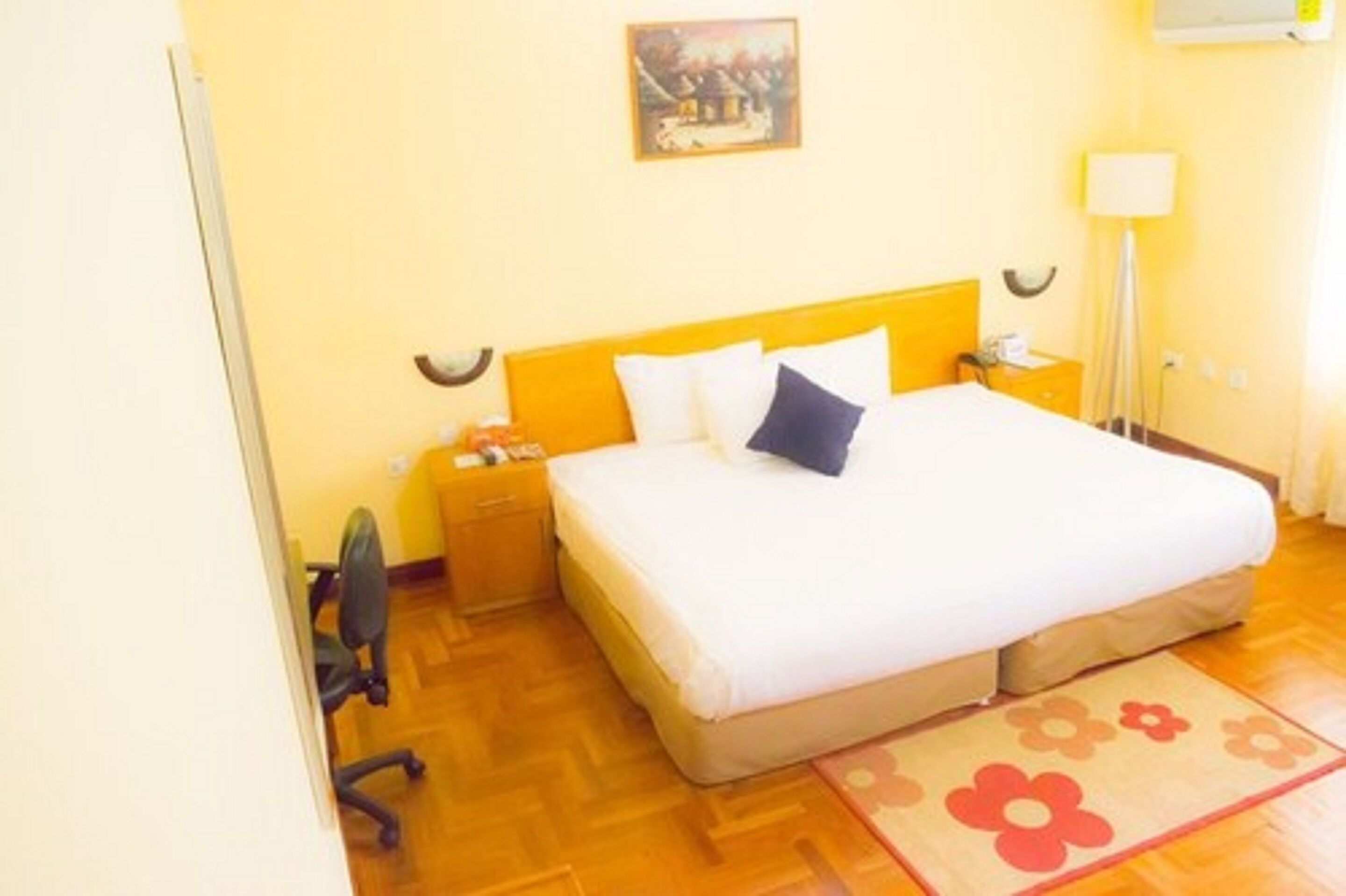 Un dormitorio con cama, mesita de noche, una silla, lámpara y un cuadro en la pared.