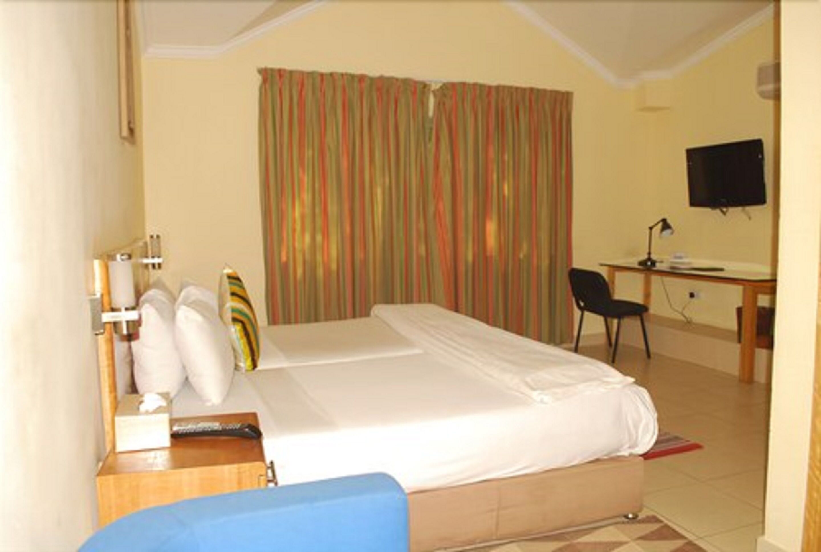 A hotel room with a bed, a desk, a chair, a television, and curtains.