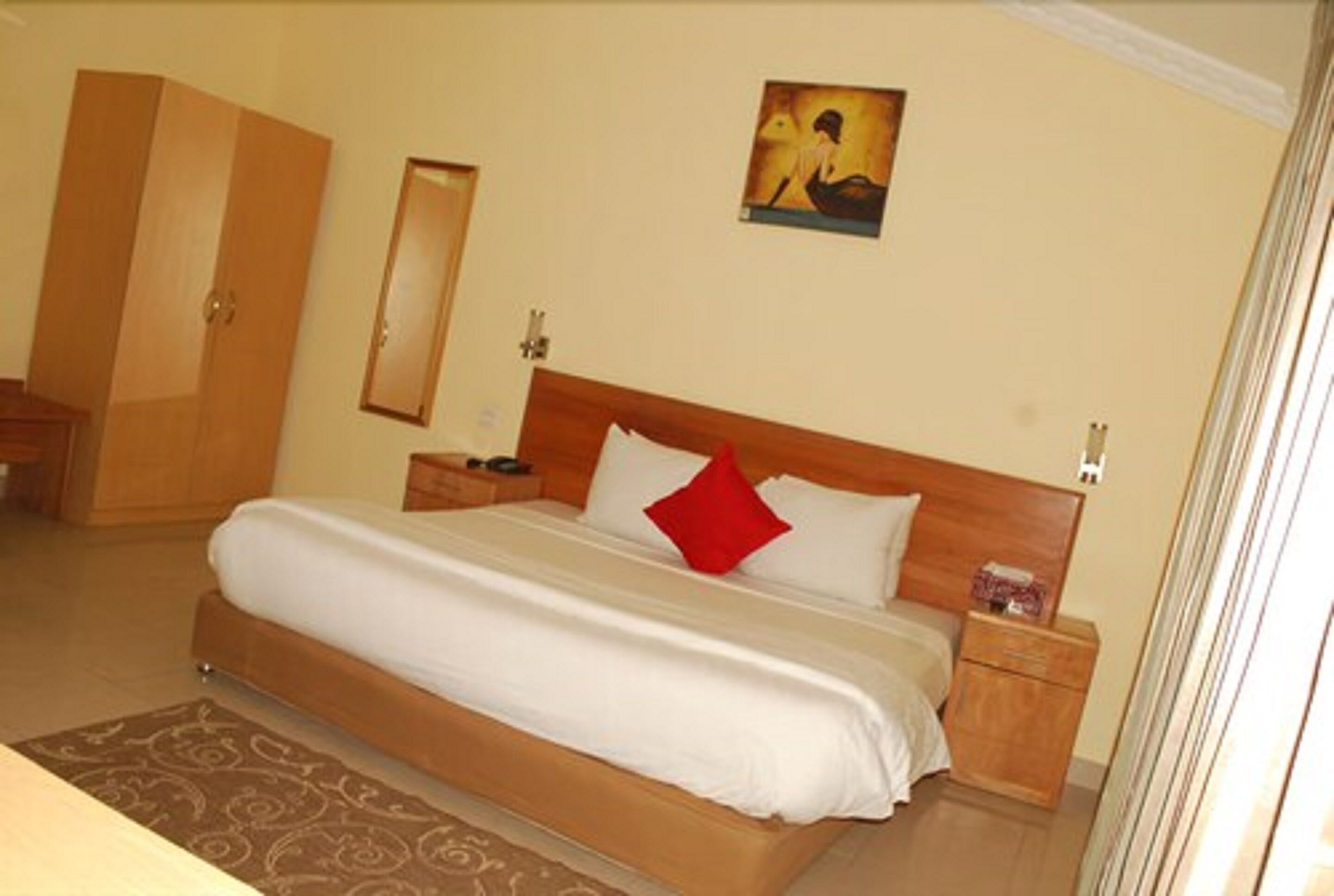 Una habitación de hotel con una cama grande, cabecera de madera, mesita de noche, armario y un cuadro en la pared.