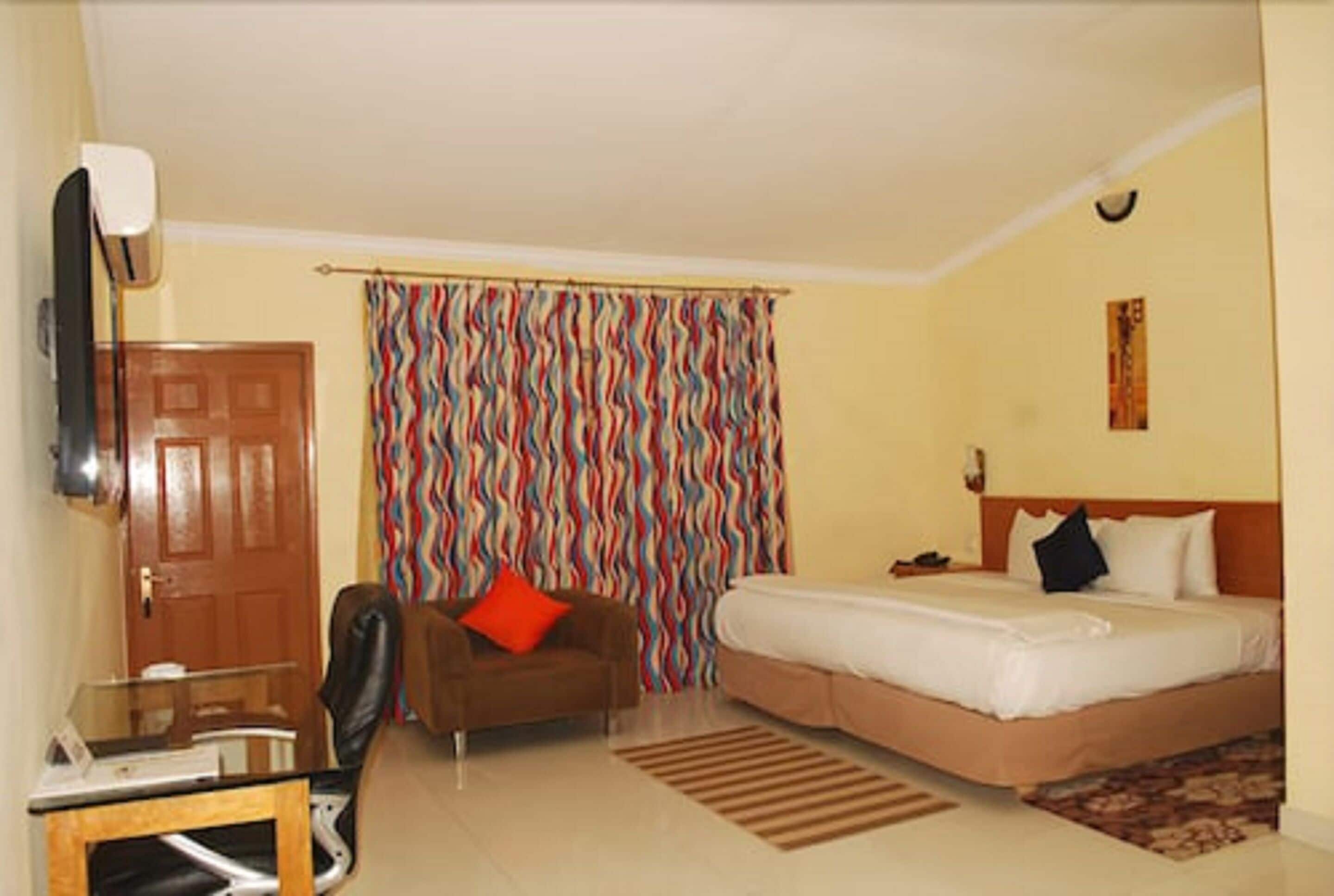 A hotel room with a bed, a sofa, a desk, and a curtain with a wavy pattern.
