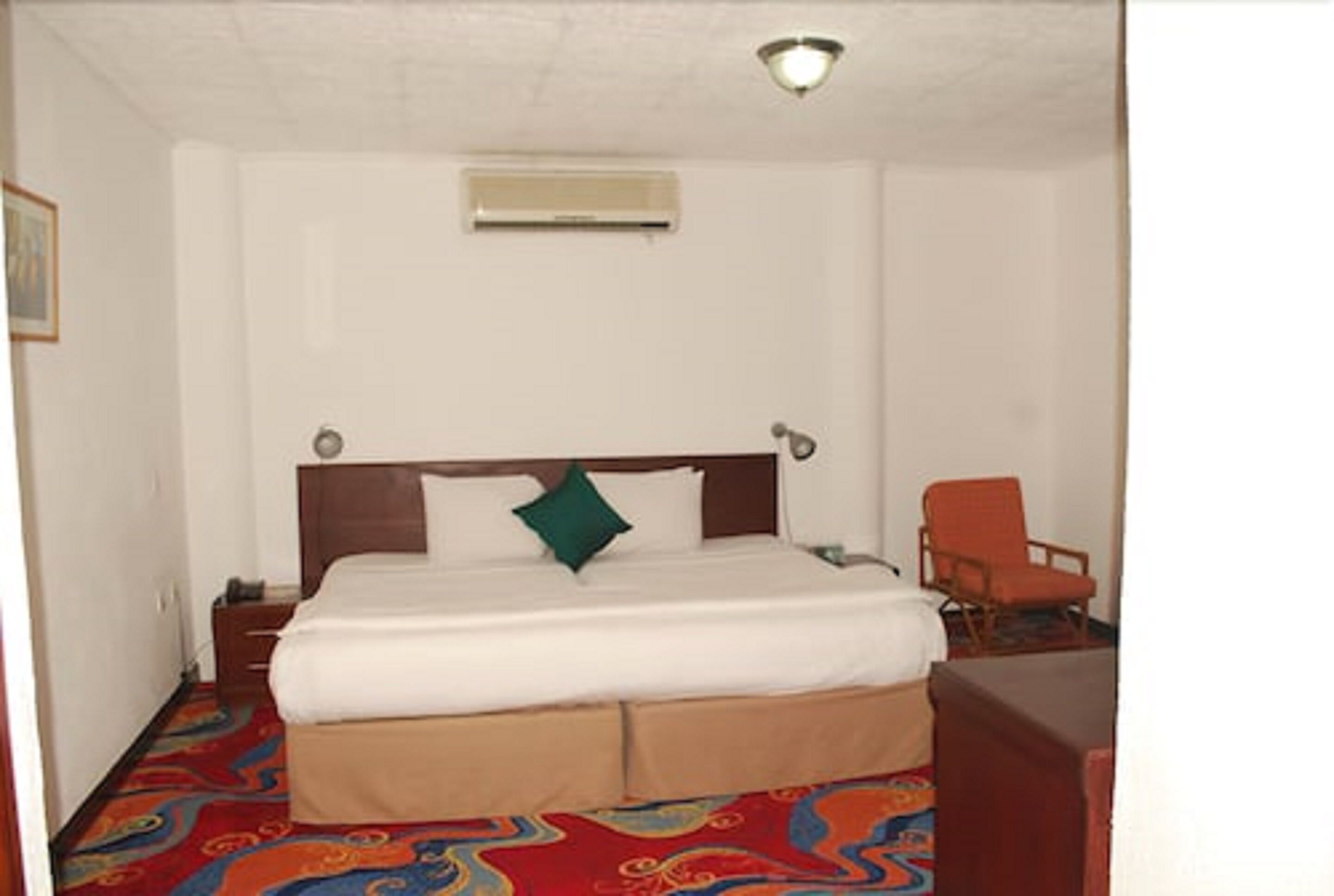 Quarto de hotel com cama, cadeira, mesa de cabeceira e ar condicionado fixado na parede.
