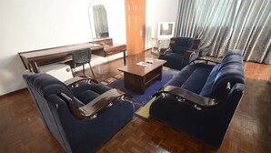 A living room with a sofa set, a coffee table, a TV, and a desk. - Airside Hotel (Accra)