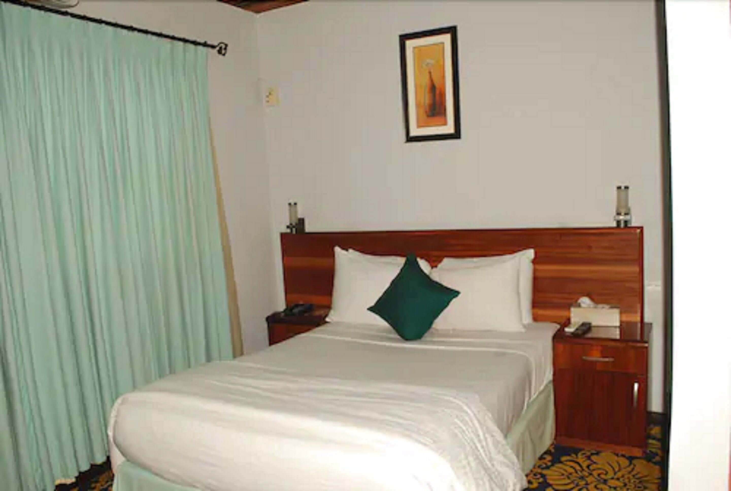 Une chambre d’hôtel avec un grand lit, une tête de lit en bois, une table de chevet avec un téléphone et un tableau encadré au mur.