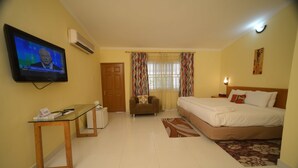A hotel room with a bed, a TV mounted on the wall, a desk, and a window with curtains. - Airside Hotel (Accra)