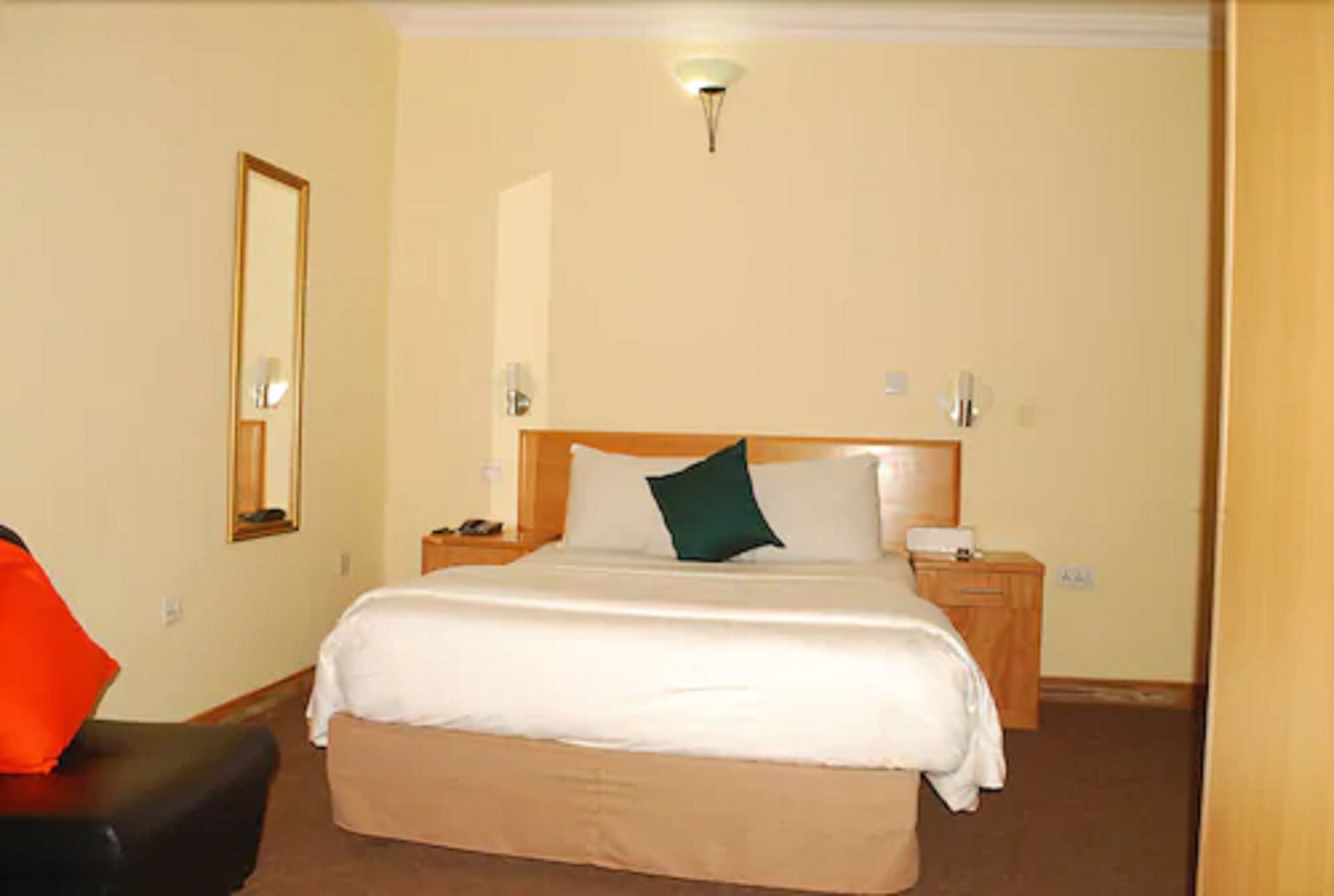 Quarto de hotel com uma cama grande, mesa de cabeceira, uma cadeira e um espelho na parede.