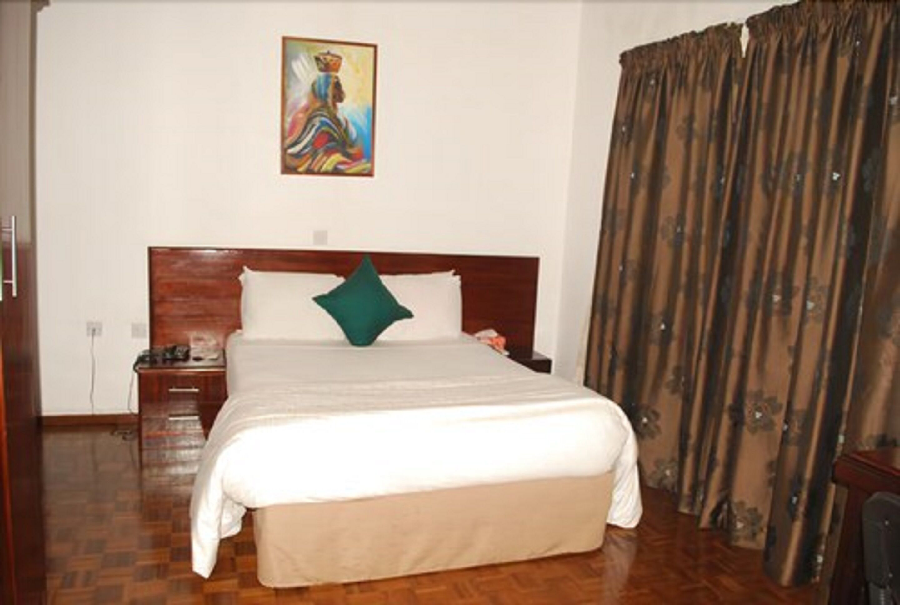 A hotel room with a large bed, a wooden headboard, a nightstand, a telephone, and a painting on the wall.