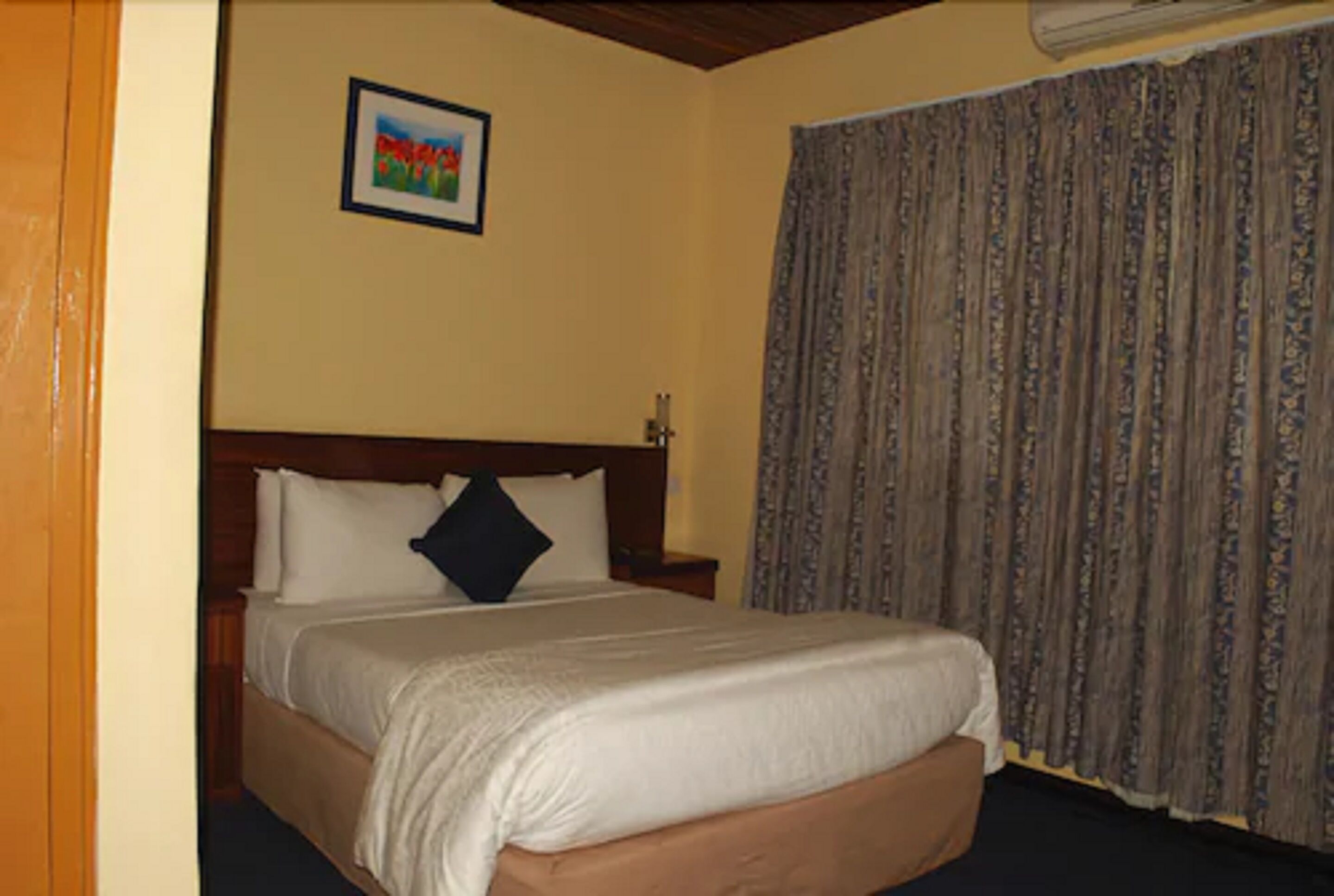 A hotel room with a large bed, a wooden headboard, a nightstand, and a curtain.
