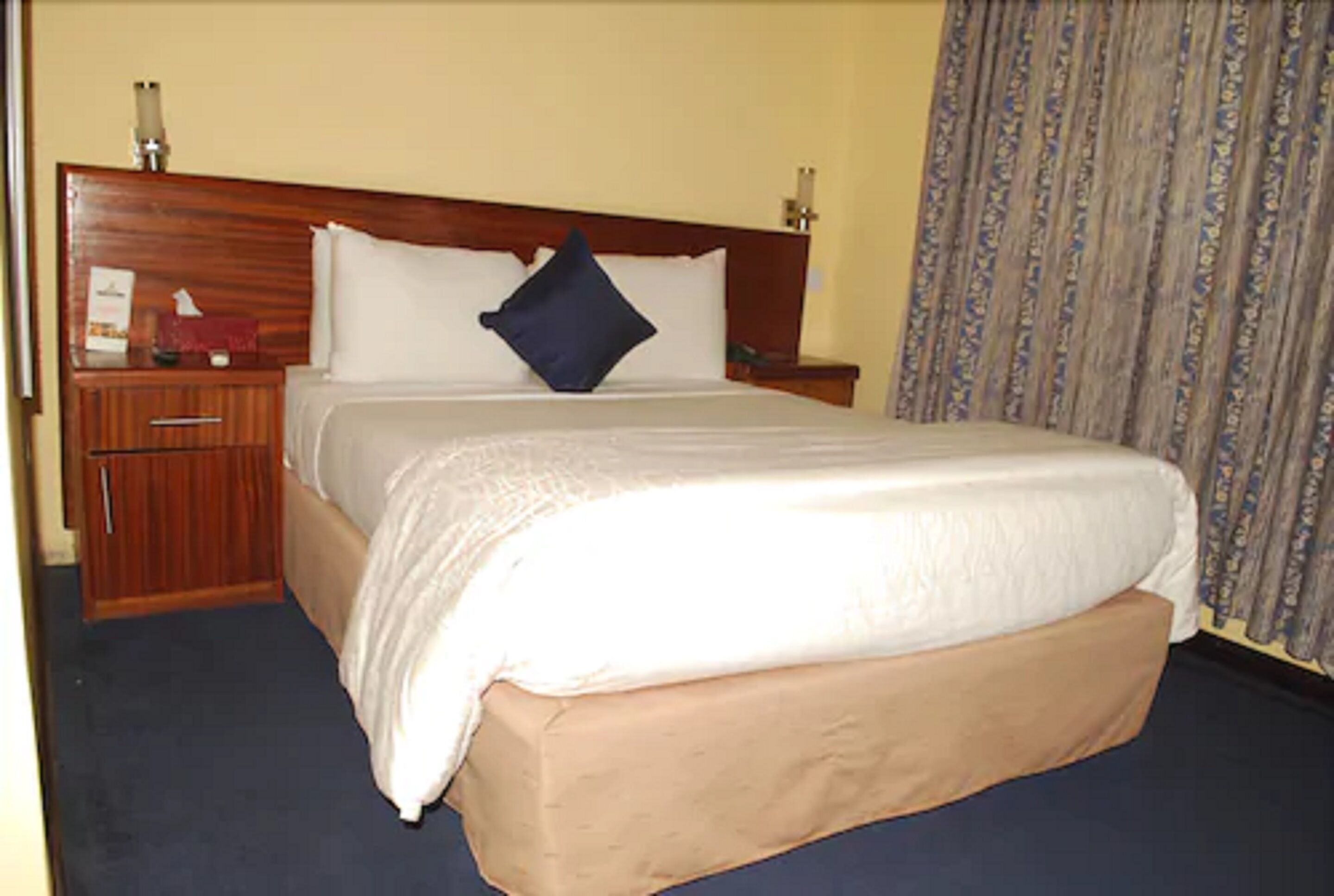Una habitación de hotel con una cama grande, cabecera de madera, una mesita de noche y una mesilla.