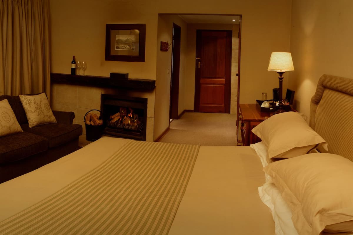 A hotel room with a bed, a sofa, a television, a fireplace, and a lamp.