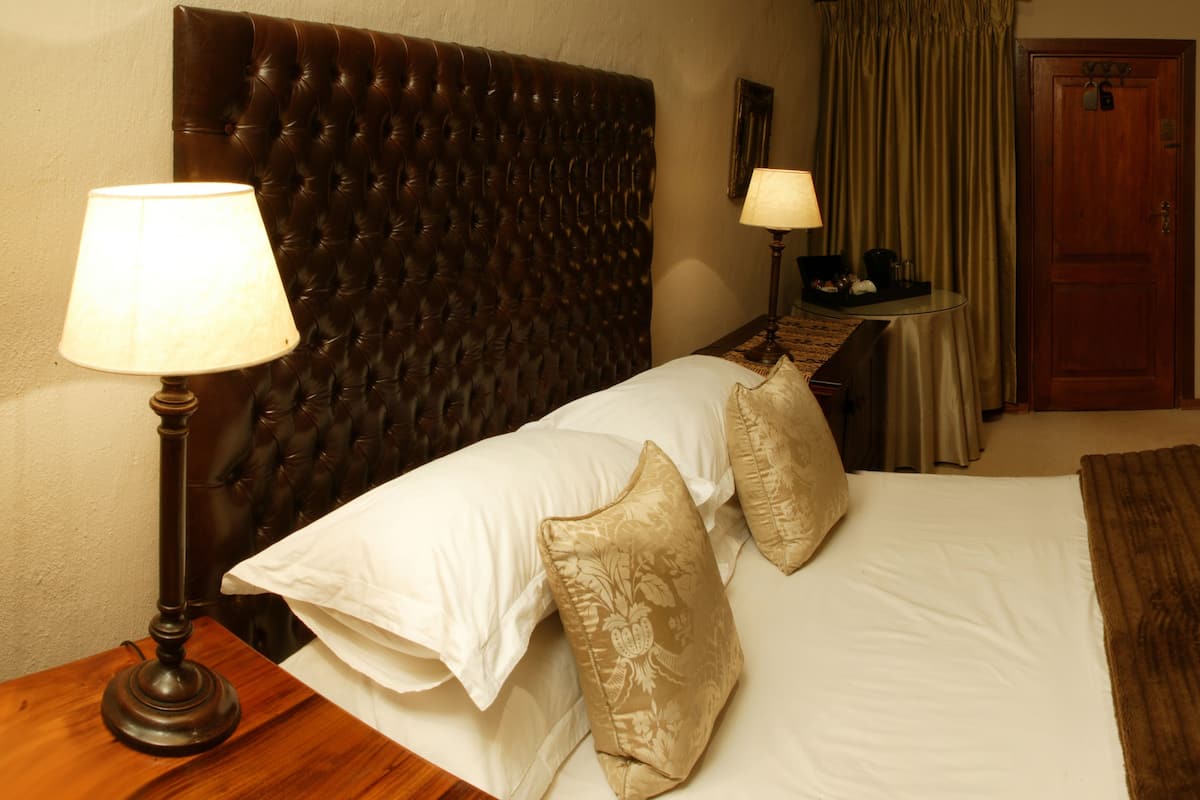 A hotel room with a large bed, two bedside lamps, a wooden nightstand, a small table with a lamp, a door, and a curtain.