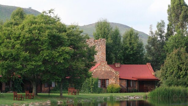Un edificio de piedra con techo rojo, rodeado de árboles y un estanque.
