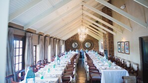 Un amplio comedor con techos altos y candelabros, con varias mesas y sillas dispuestas para un banquete.
