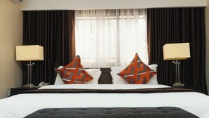 Una habitación de hotel con una cama grande, dos mesitas de noche, un teléfono y una ventana con cortinas.