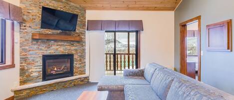 A cozy living room with a stone fireplace, a large window, and a comfortable sofa.