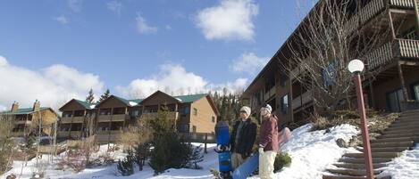 A snow-covered outdoor area with a wooden building featuring balconies and a staircase.