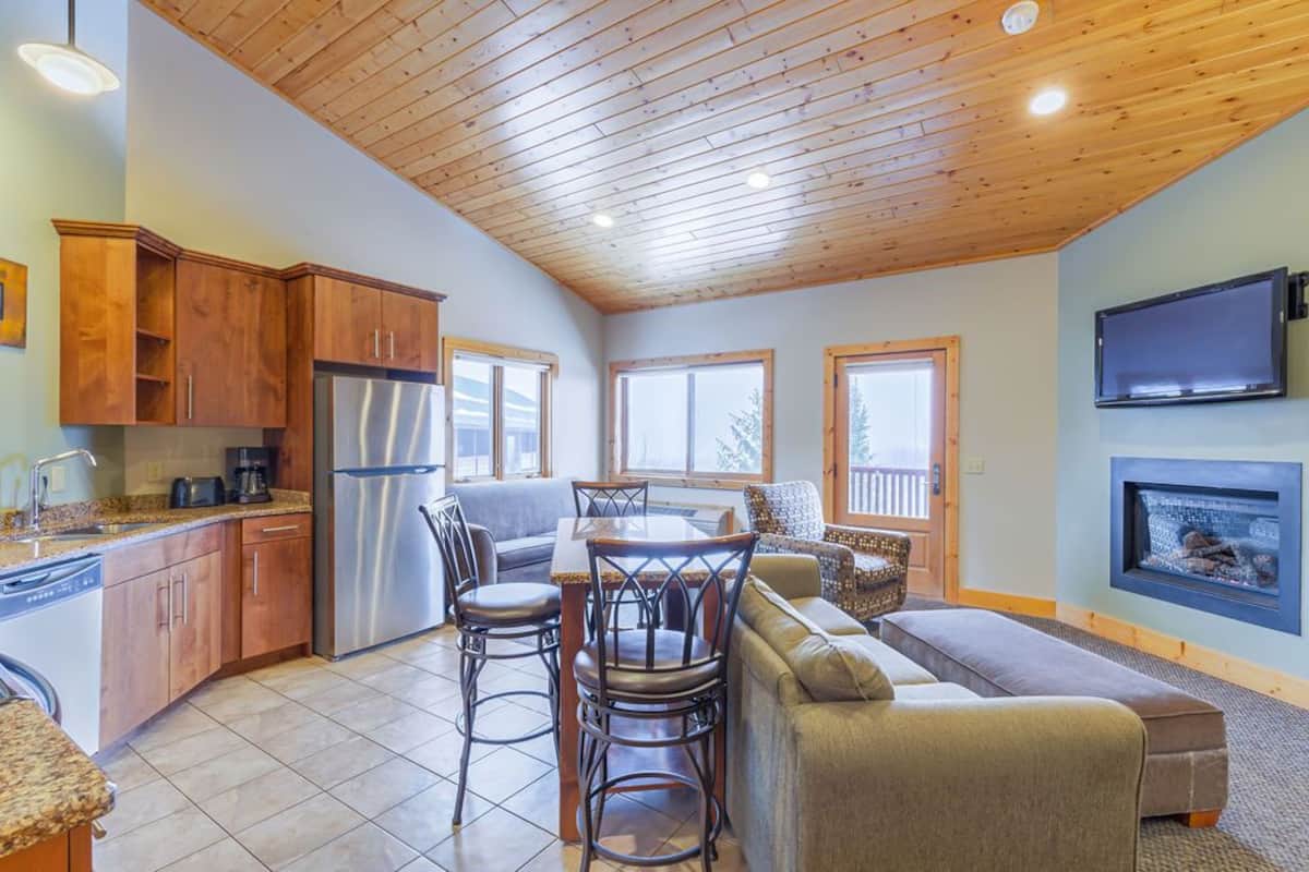 A modern kitchen with wooden cabinets, a stainless steel refrigerator, and a dining area with a table and chairs.