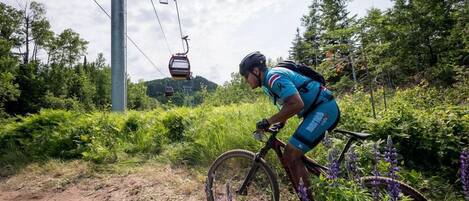 A cyclist on a dirt path with a cable car in the background.