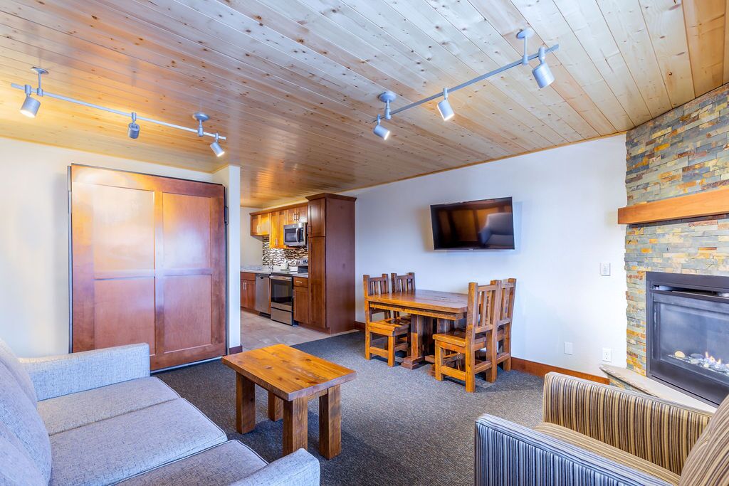 A spacious living area with a fireplace, a dining table, and a kitchen in the background.