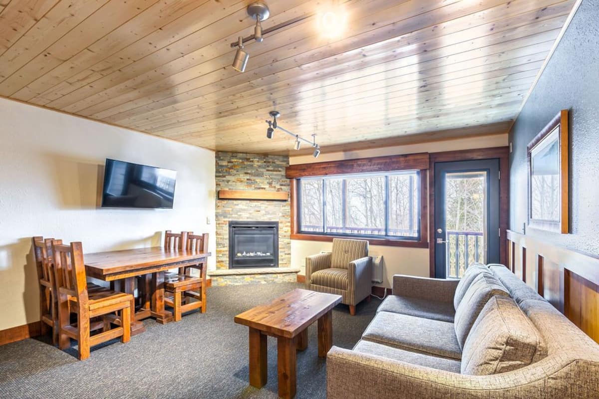 A cozy living room with a fireplace, wooden furniture, and a television mounted on the wall.