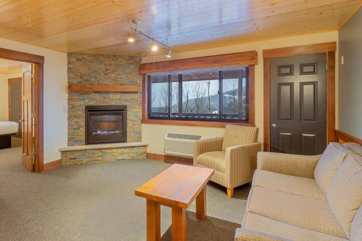 A cozy living room with a fireplace, a large window, and a door.