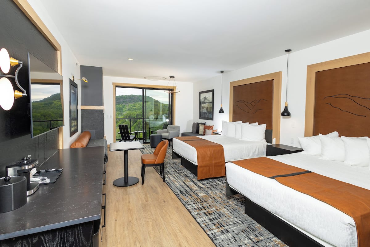 A modern hotel room with two beds, a desk, and a large window offering a mountain view.