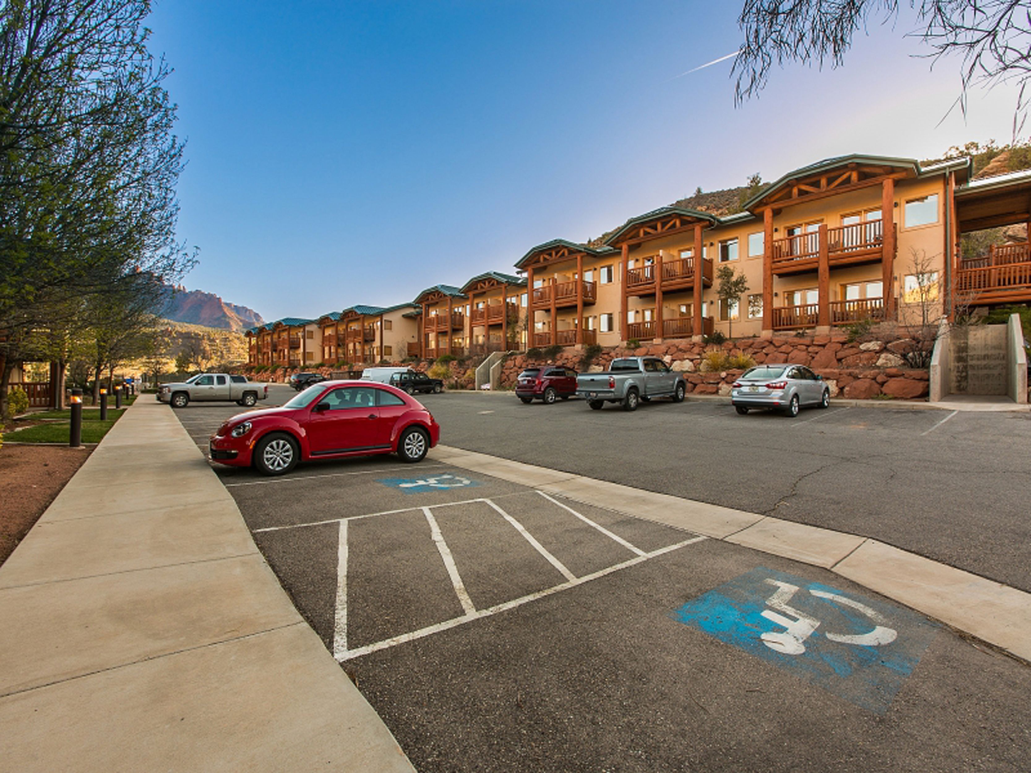 A parking lot with a red car parked in a handicapped space, surrounded by multi-story buildings with balconies.