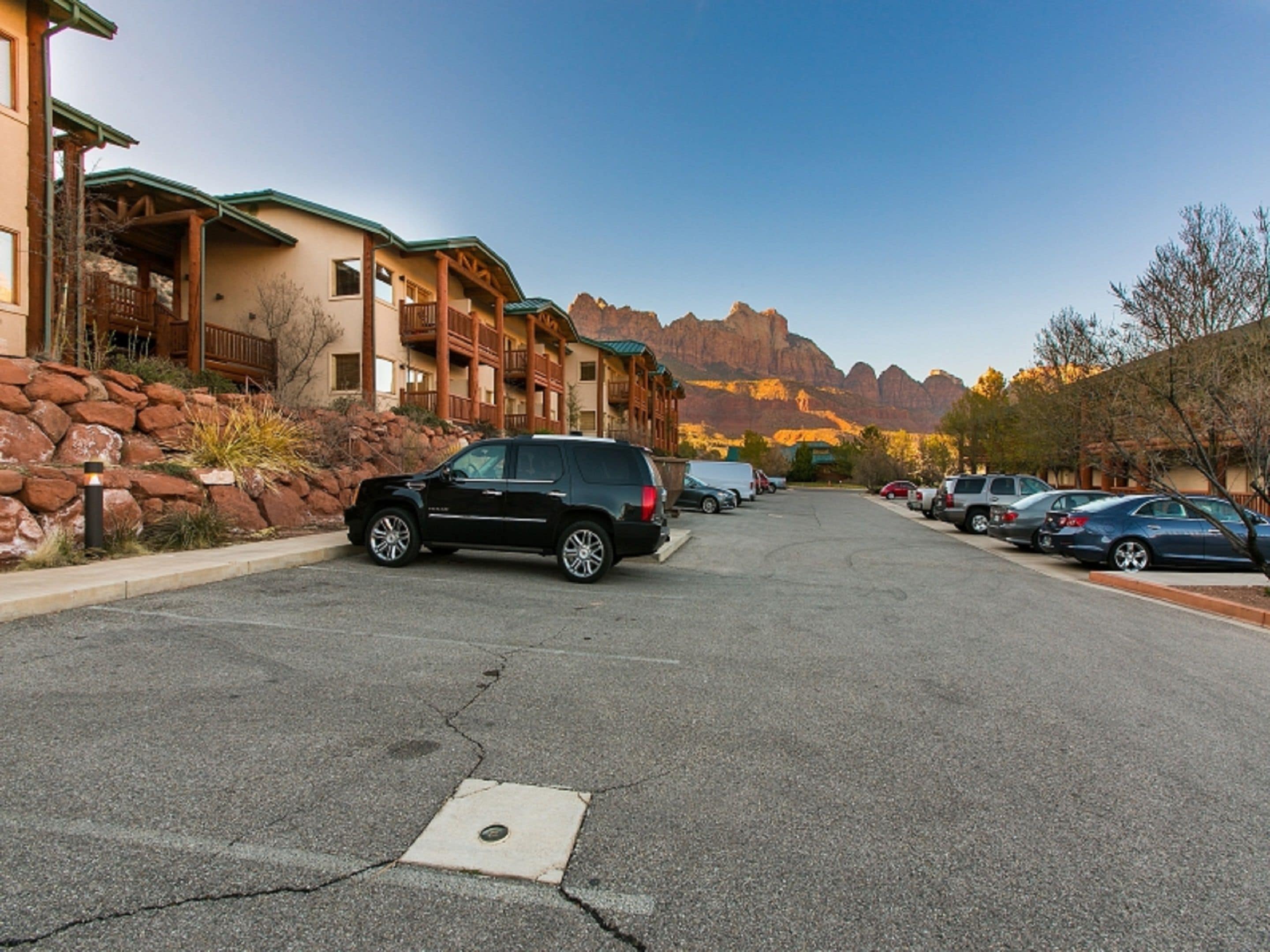 Un parcheggio con diverse auto, un edificio con un balcone e montagne sullo sfondo.