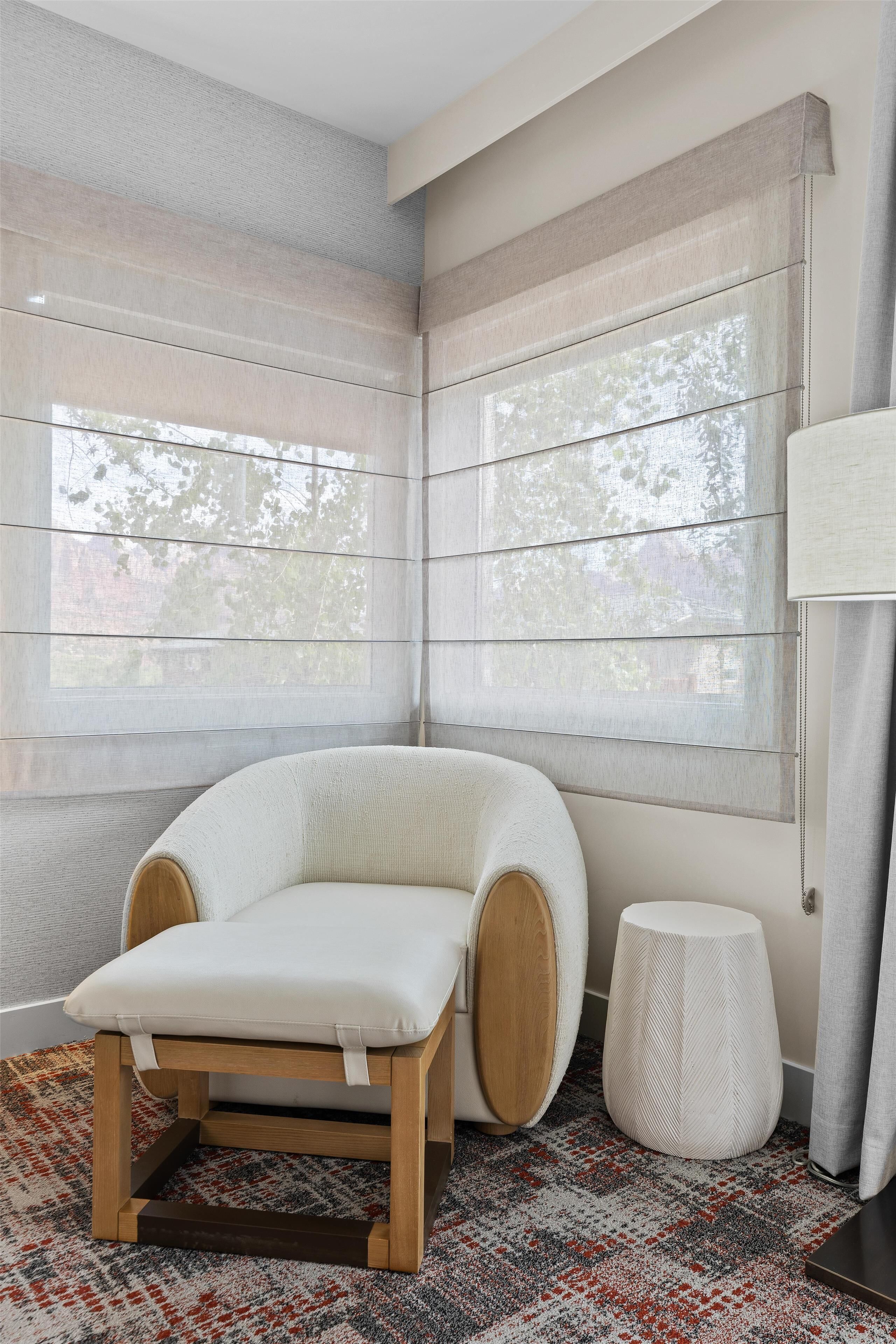 A corner room with a cushioned chair, a small round stool, and a patterned rug.