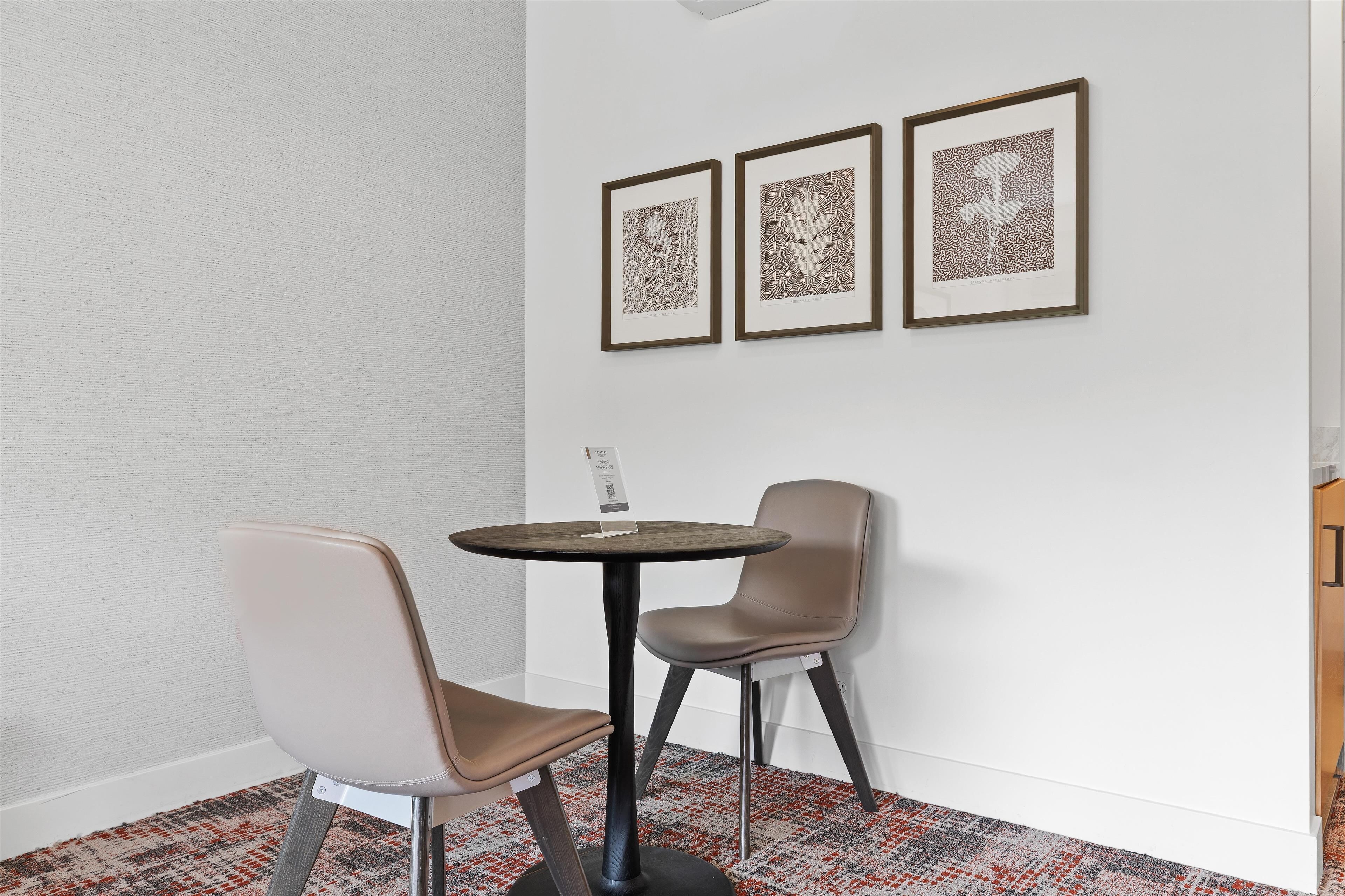 A small, modern room with a round table and two chairs, a patterned rug, and three framed artworks on the wall.