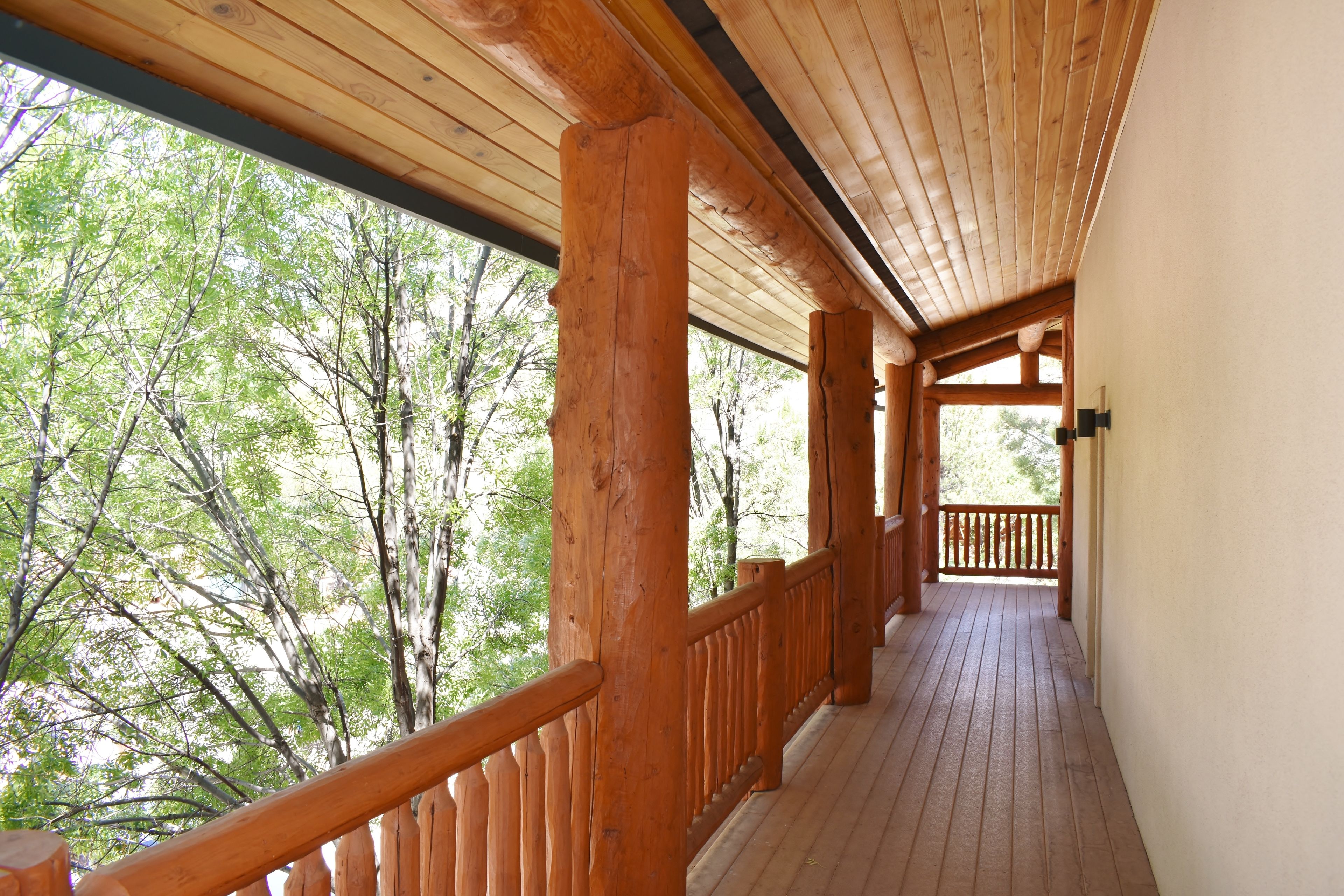 A wooden deck with a railing, leading to a covered area with a view of trees.
