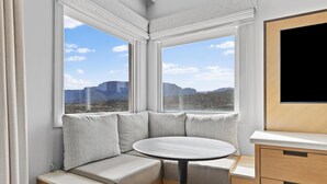 A corner seating area with a round table, a cushioned bench, and a view of mountains through large windows.