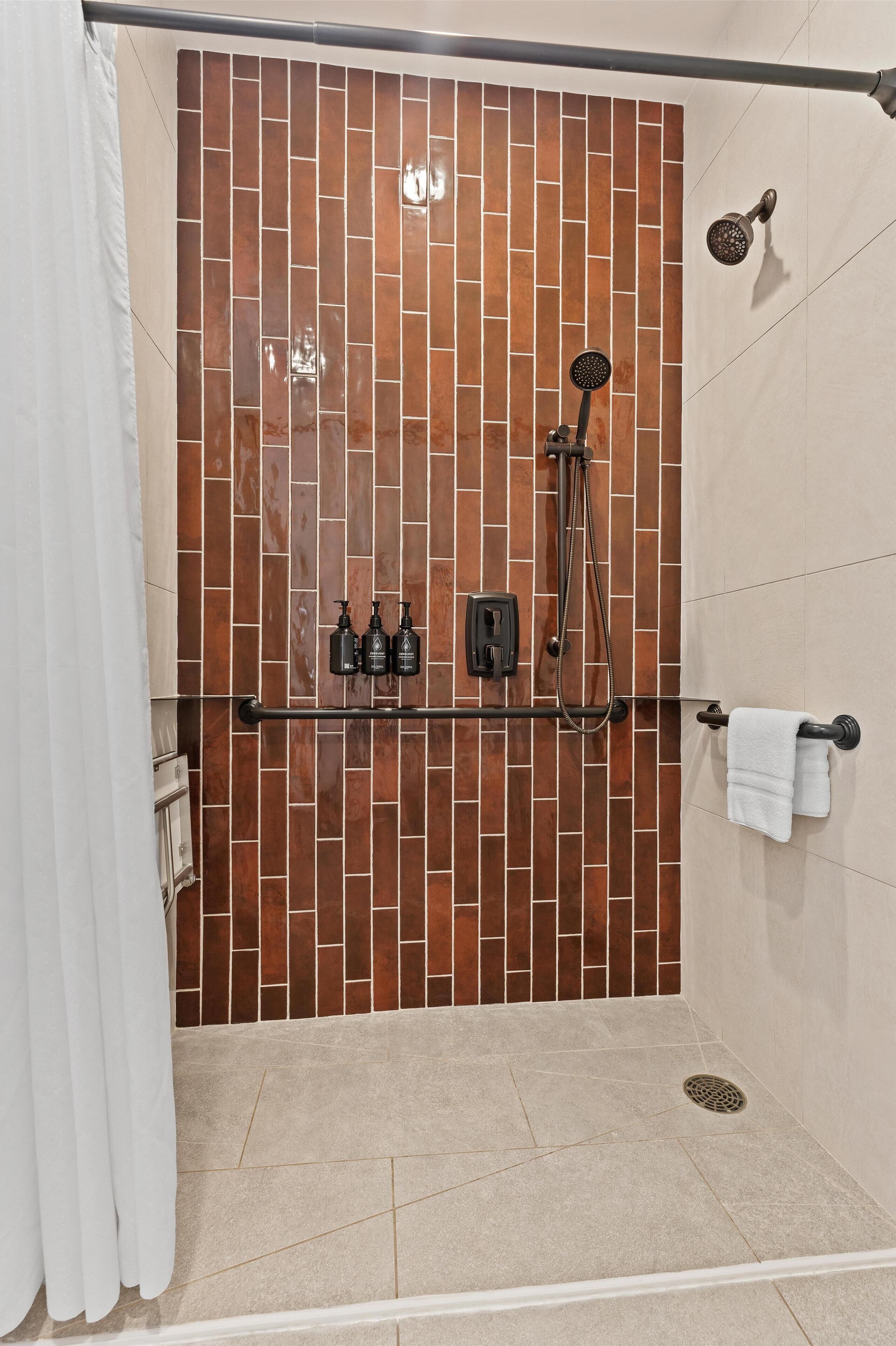 Un espace douche avec un mur carrelé, une douchette à main, un porte-serviettes et un étagère pour produits de douche.