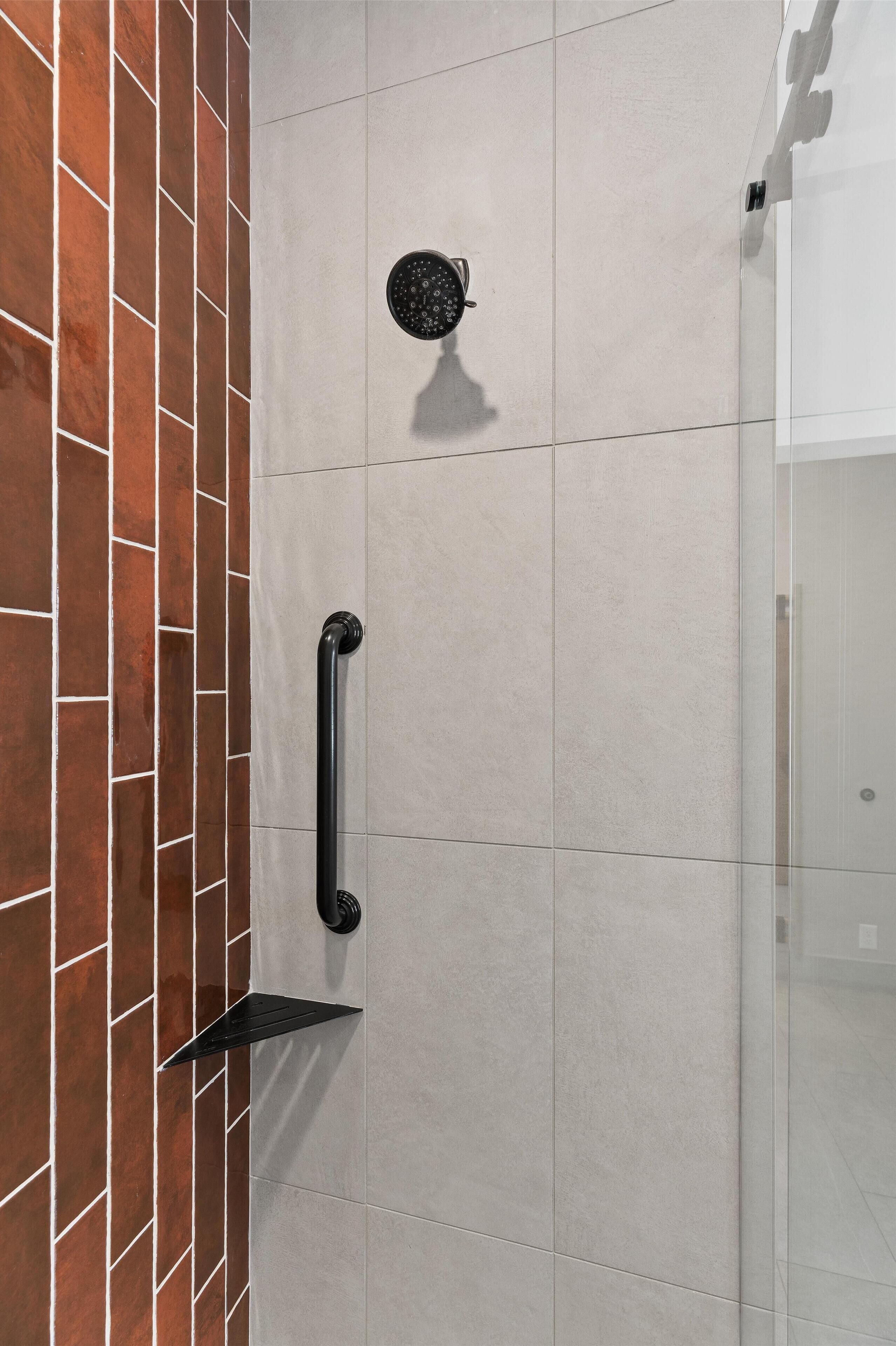 Douche met een zwarre handgreep, een ronde douchekop en een glazen deur.