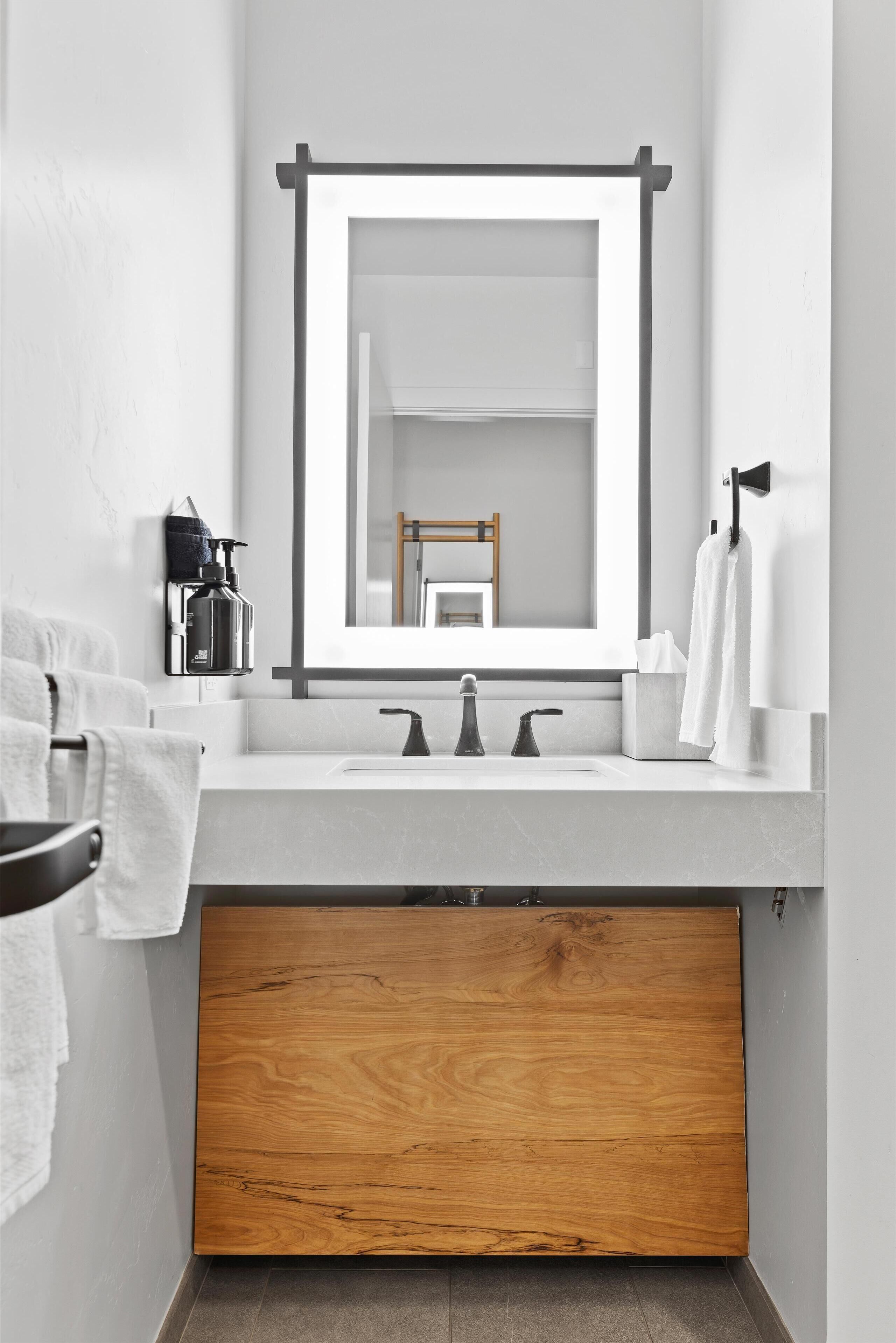 A modern bathroom with a wooden vanity, a large mirror, and a white sink.
