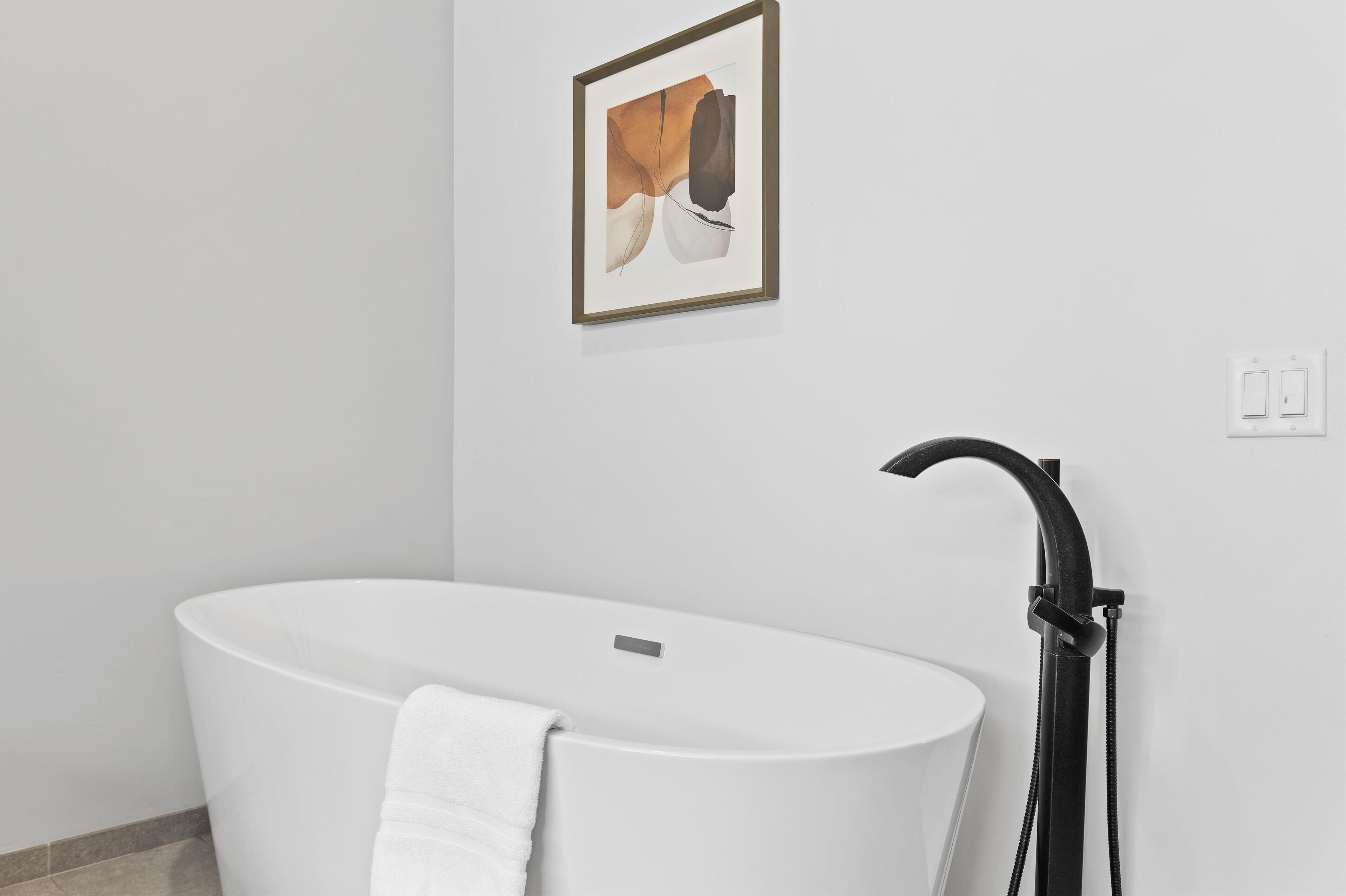 A modern bathroom with a freestanding bathtub, a towel, and a framed artwork on the wall.