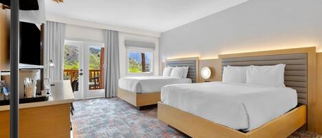 A hotel room with two beds, a desk with a coffee machine, and a view of the outdoors.
