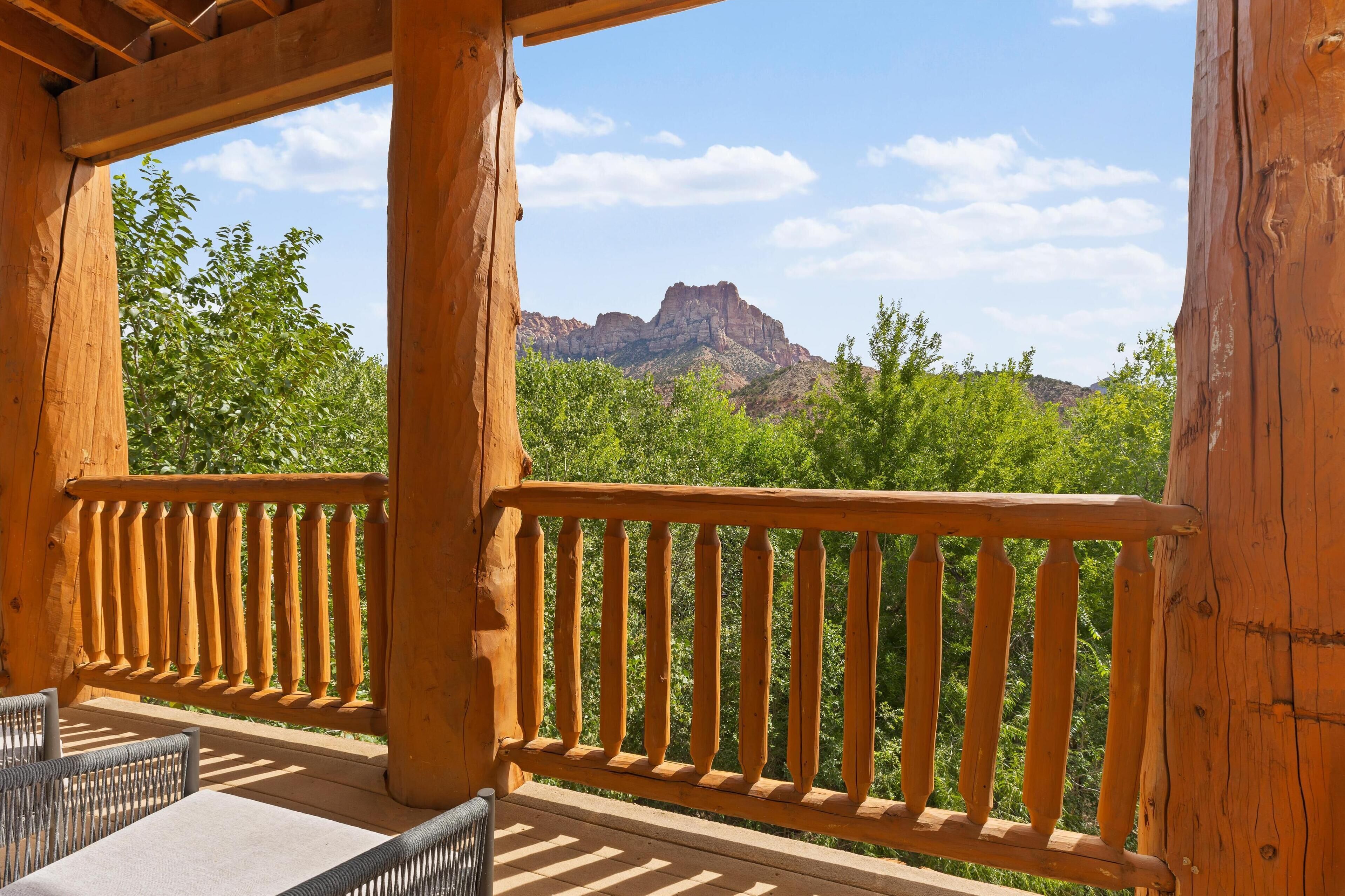 A wooden balcony with a view of green trees and a mountain.