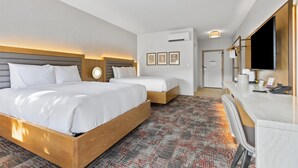A hotel room with two beds, a desk, a mirror, and a patterned carpet.