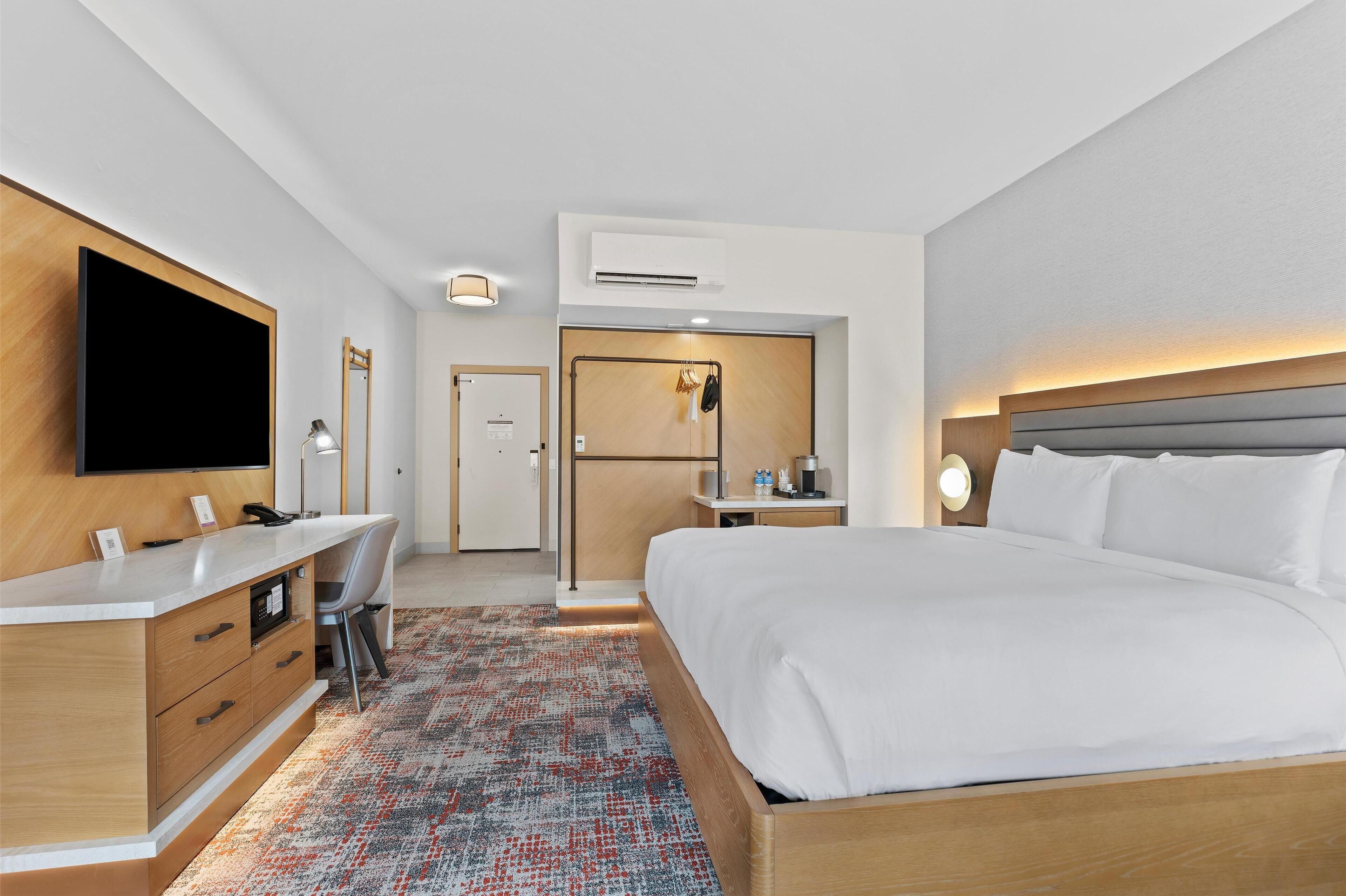 Een hotelkamer met een bed, bureau, stoel, televisie en een kleine kitchenette.
