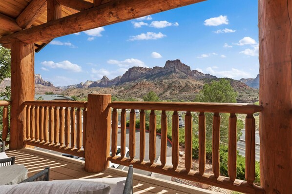 A wooden balcony with a view of a mountainous landscape and a parking area.