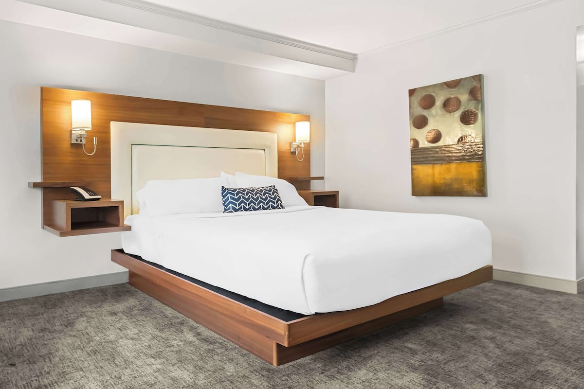 Une chambre d’hôtel moderne avec un grand lit, une tête de lit en bois, des tables de chevet avec des lampes et un élément décoratif mural.