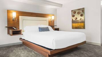 A modern hotel room with a large bed, wooden headboard, bedside tables with lamps, and a decorative wall piece.