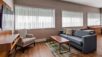 A living room with a sofa, armchair, coffee table, and a TV mounted on the wall.
