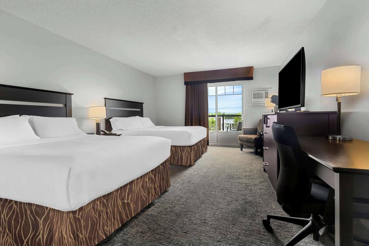 Une chambre d’hôtel avec deux lits, un bureau avec une chaise, une télévision et une vue sur l’extérieur.