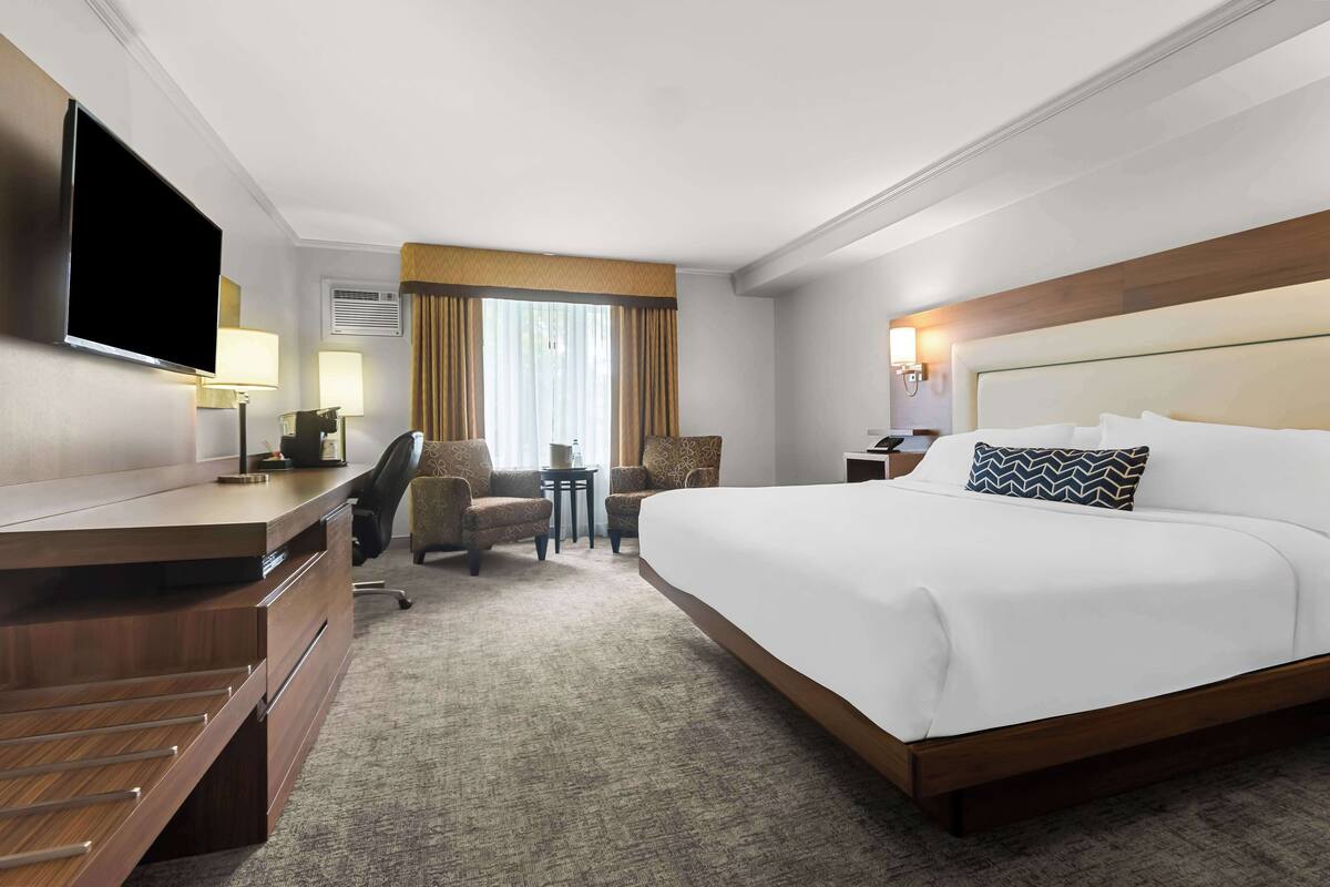 Une chambre d’hôtel avec un grand lit, un bureau doté d’un téléviseur à écran plat, deux fauteuils, une petite table et une fenêtre avec des rideaux.