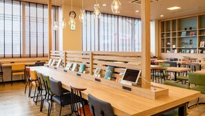 A modern library with wooden tables and chairs, bookshelves, and hanging light fixtures. - Comfort Hotel Hamamatsu (Hamamatsu)