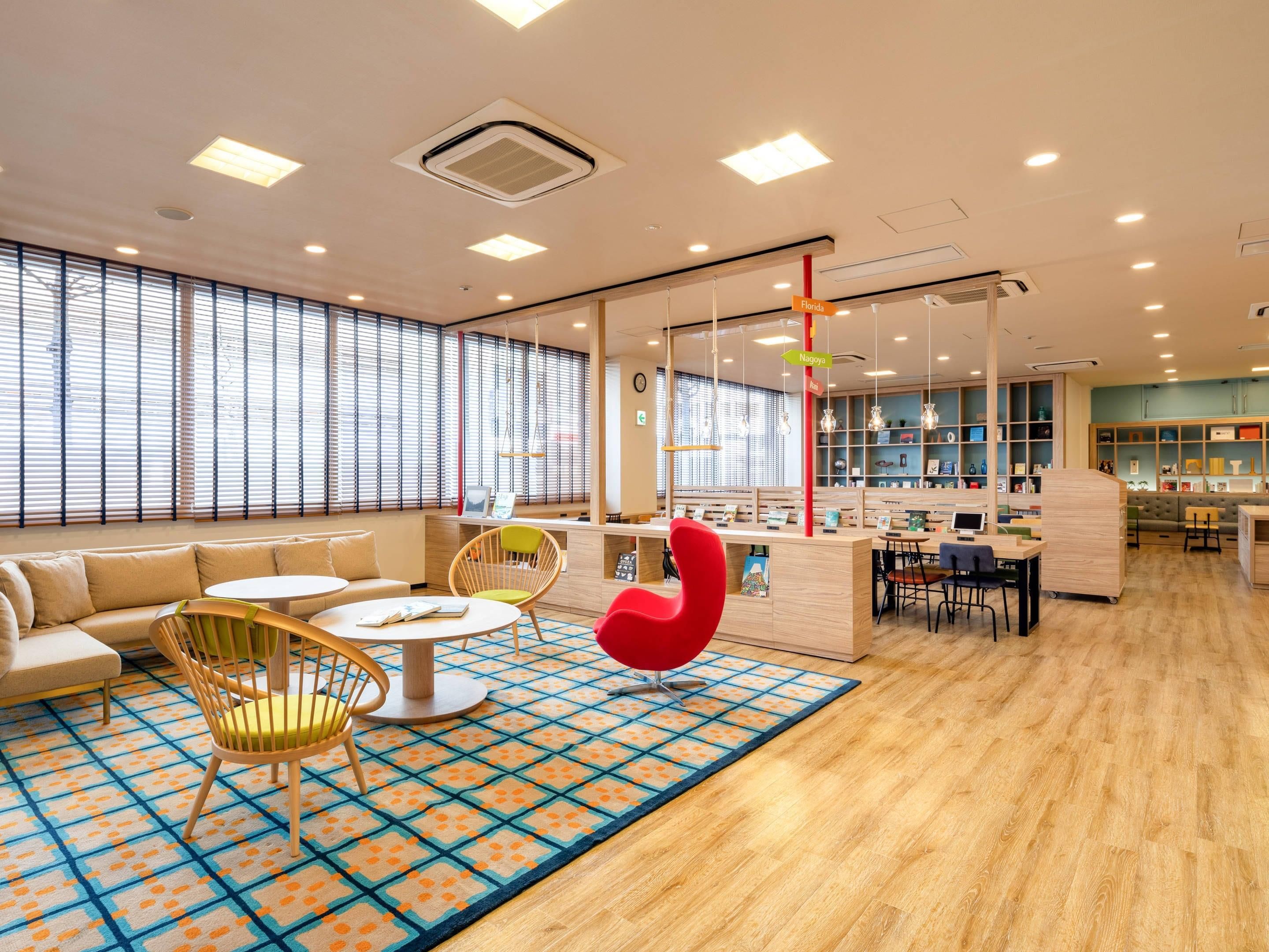 A modern library with a central reading area, individual study tables, and a large window with blinds.